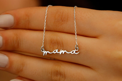 A dainty necklace with the inscription 'mama' worn by a person with a white top.