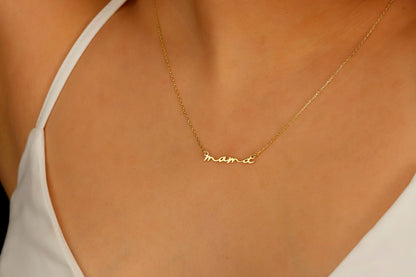 A dainty necklace with the inscription 'mama' worn by a person with a white top.