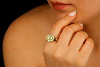 A close-up image of a person's finger wearing a college seal engraving signet ring.