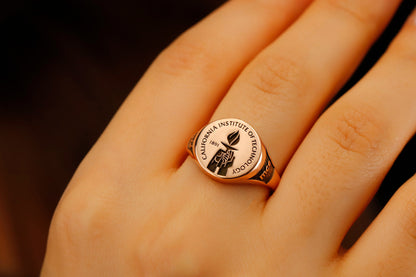 A close-up image of a person's finger wearing a college seal engraving signet ring.