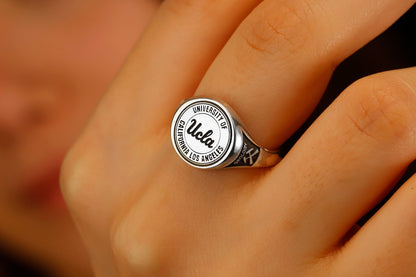 A close-up image of a person's finger wearing a college seal engraving signet ring.