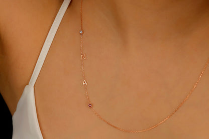 A close-up image of a sterling silver necklace with gold lettering and multicolored birthstones laid out on a person's neck.