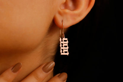 A close-up image of a woman's ear wearing a rose gold dangle earring with angel number '999' inscribed.