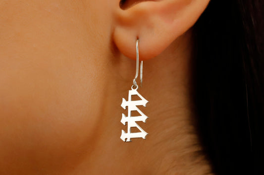 A close-up image of a woman's ear wearing a silver dangle earring with angel number 444 inscribed.