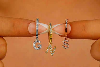 A close-up image of 3 dangle initial earrings with a capital letter 'G' 'N' 'S'.