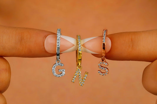 A close-up image of 3 dangle initial earrings with a capital letter 'G' 'N' 'S'.
