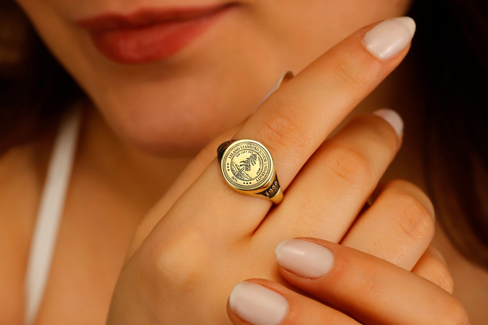 A close-up image of a person's finger wearing a college seal engraving signet ring.
