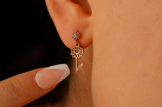 A close-up image of a woman's ear wearing a dangle birth month flower earring with a birthstone.