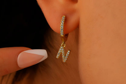 A close-up image of a woman's ear wearing a gold dangle initial earring with a capital letter 'N'.