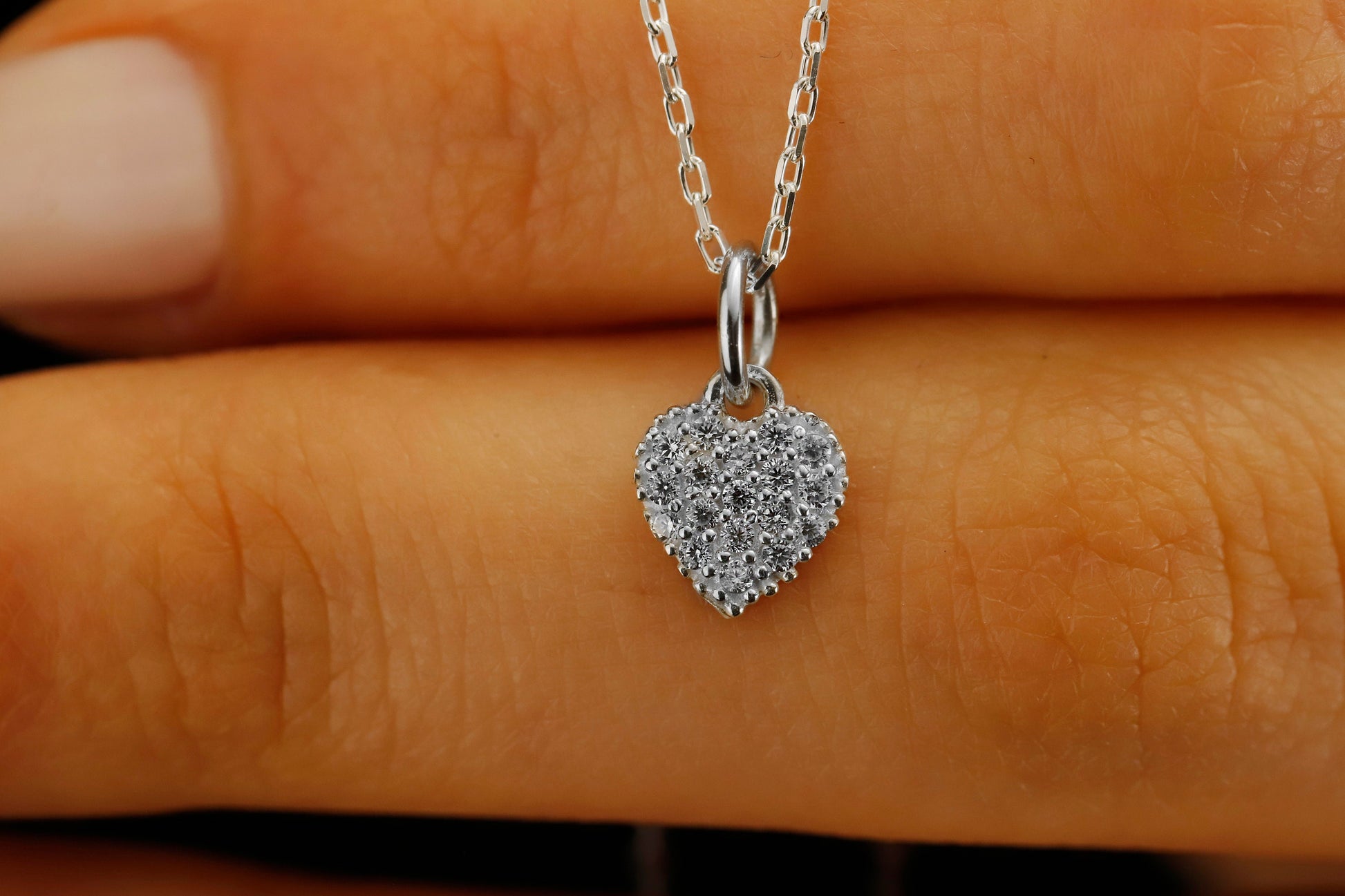 Heart-shaped silver pendant with clear stones on a hand