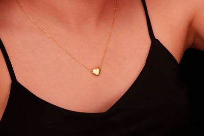 
A gold finish, heart-shaped pendant hangs from a thin gold chain on a person's neck. A product by SilverGoldandRose.com.