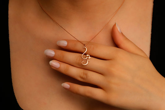 Hand holding a delicate gold necklace with a unique pendant against a dark background