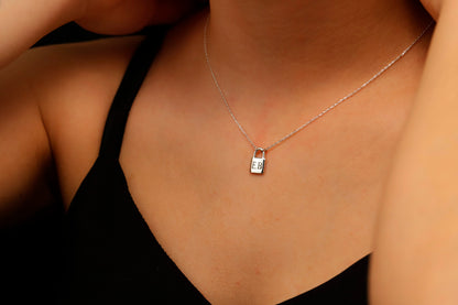 A close-up image of a person wearing a padlock-shaped pendant necklace in gold color, attached to a chain.