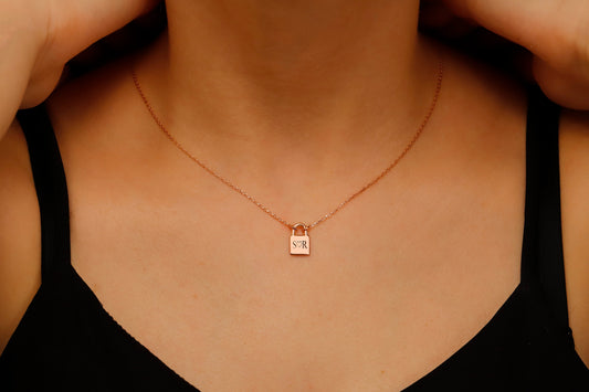 A close-up image of a person wearing a padlock-shaped pendant necklace in gold color, attached to a chain.