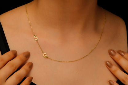 A close-up image of a dainty sideways initial necklace worn by a person, with a hand adjusting the necklace.