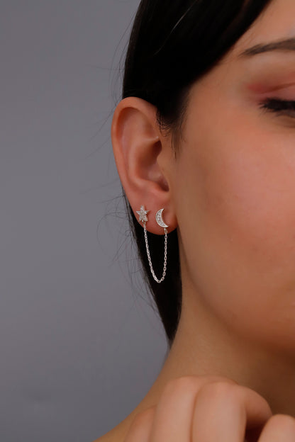 A close-up image of a person wearing 925 sterling silver pave star and moon earrings with small dangling earrings on the lobes of their ears.