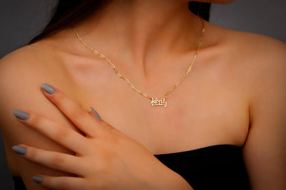 A woman wearing a black dress showcasing a dainty gold-colored necklace with Chinese characters on it.