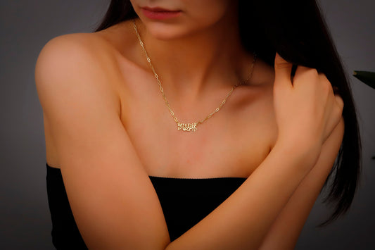 A woman wearing a black dress showcasing a dainty gold-colored necklace with Chinese characters on it.