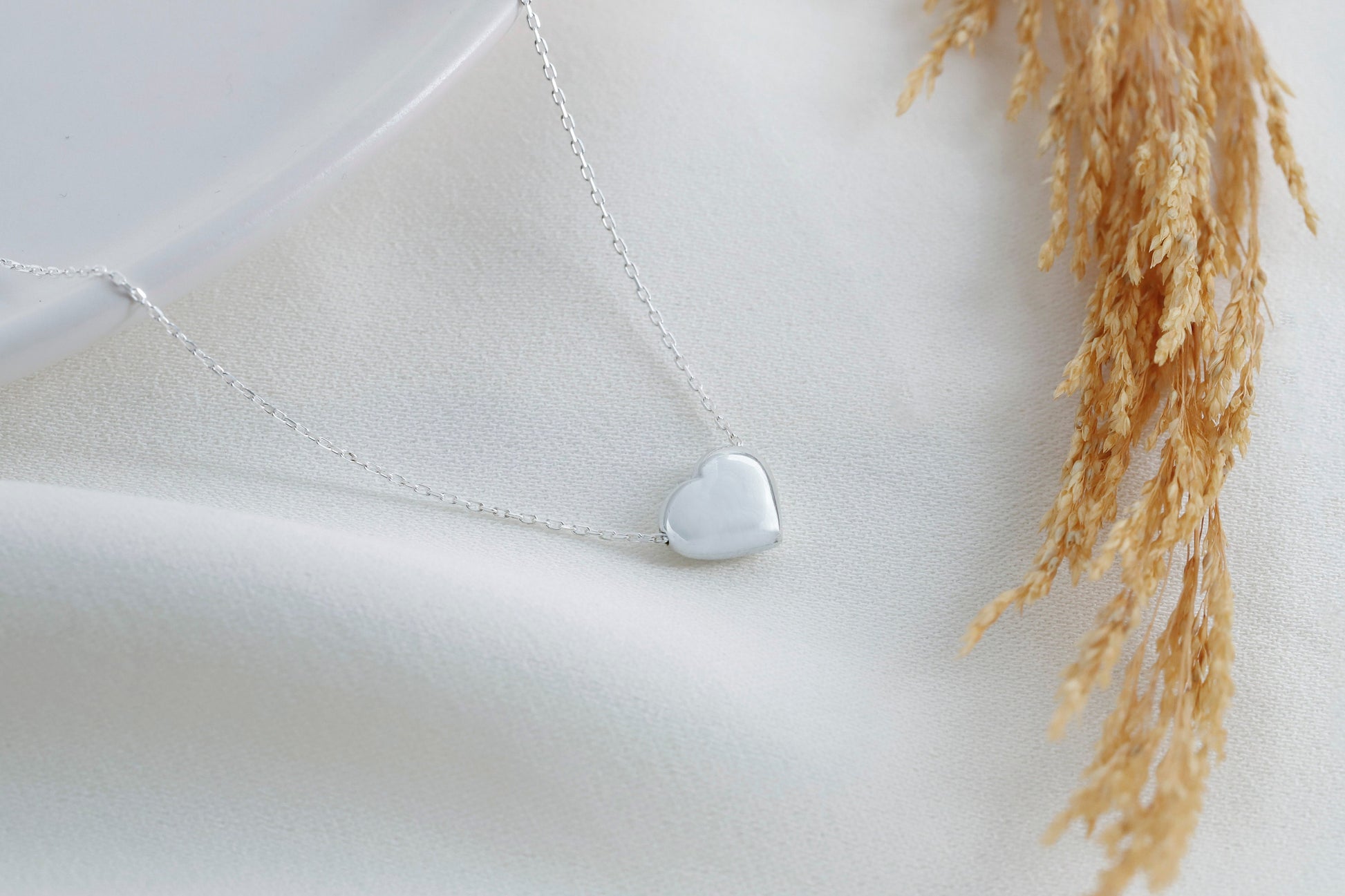 
A silver, heart-shaped pendant hangs from a thin silver chain. A product by SilverGoldandRose.com.