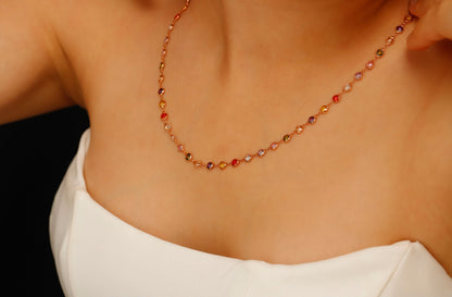 A multicolor baguette cut gemstone necklace with a rose gold finish, displayed on a person's neck.