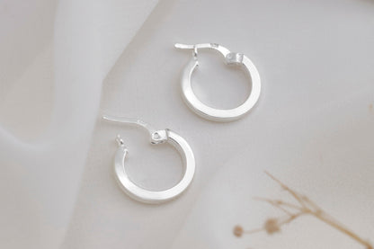 A close-up image of a person wearing small gold hoop earrings, with a focus on the earrings.