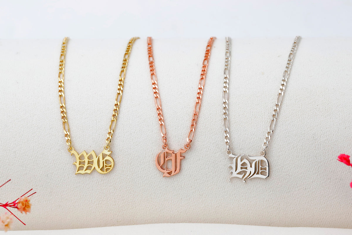 Three gold necklaces with different letter pendants on a white surface.