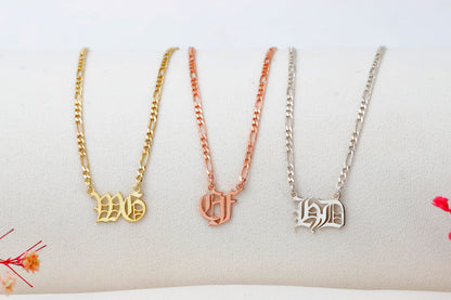Three gold necklaces with different letter pendants on a white surface.