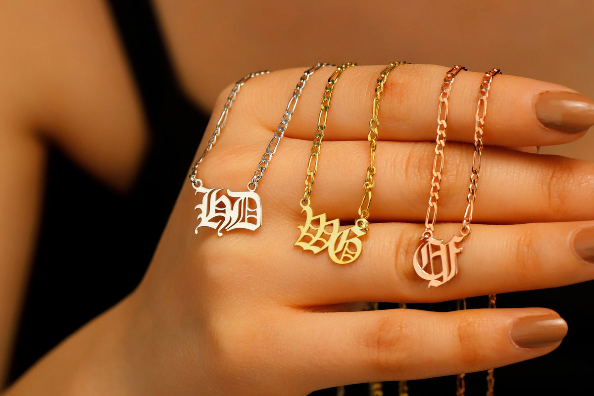 Hand holding four gold necklaces with different letter pendants against a blurred background