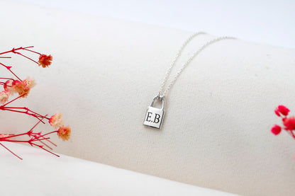 A close-up image of a person wearing a padlock-shaped pendant necklace in gold color, attached to a chain.