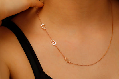 A close-up image of a dainty sideways initial necklace worn by a person, with a hand adjusting the necklace.