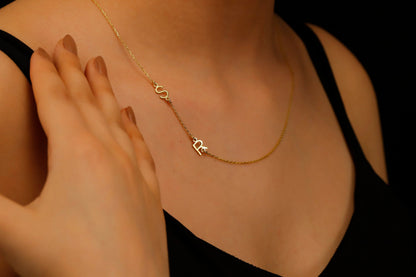 A close-up image of a dainty sideways initial necklace worn by a person, with a hand adjusting the necklace.