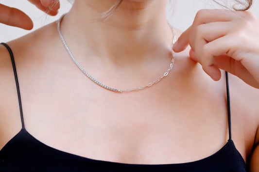 A close-up image of a person wearing a silver tennis and paperclip chain necklace.