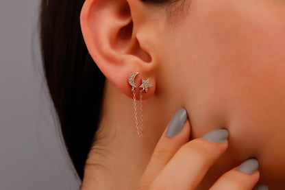 A close-up image of a person wearing gold-colored dangle earrings with star and moon designs.