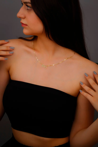 A woman wearing a black dress showcasing a dainty gold-colored necklace with Chinese characters on it.