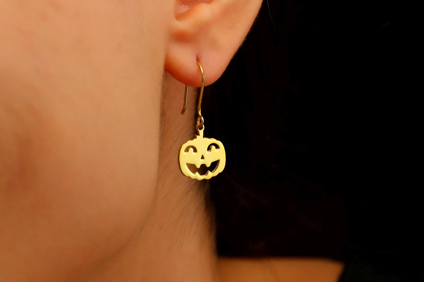 Gold pumpkin-shaped earrings worn by a person with a dark background
