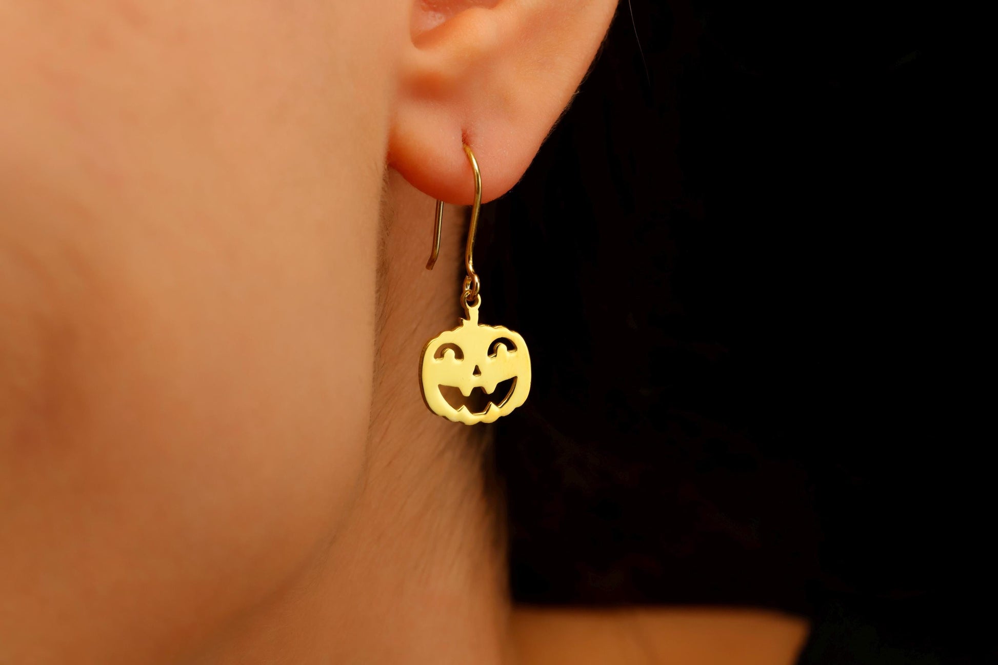 Gold pumpkin-shaped earrings worn by a person with a dark background