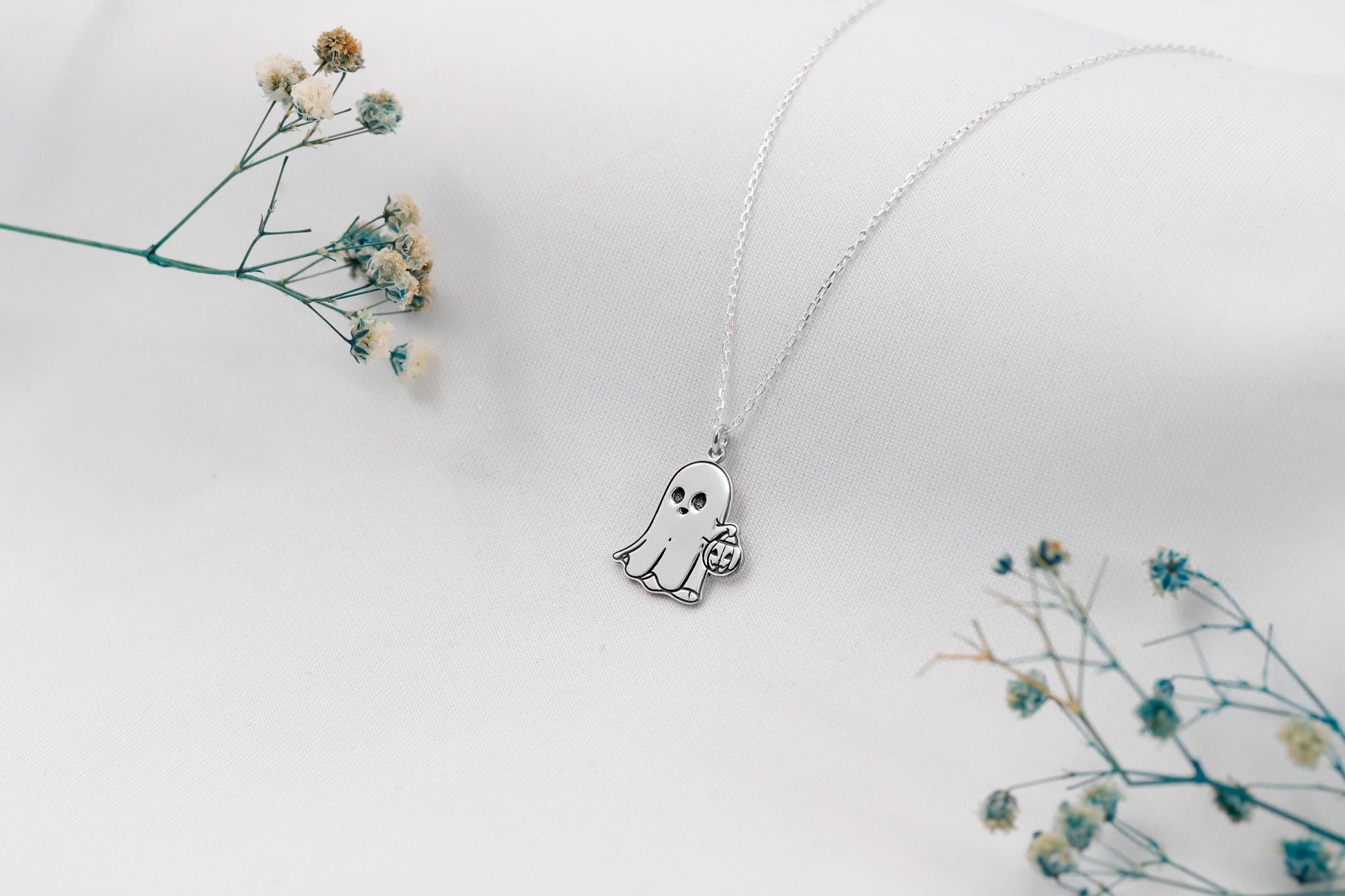 Ghost-shaped pendant necklace on a white background with dried flowers