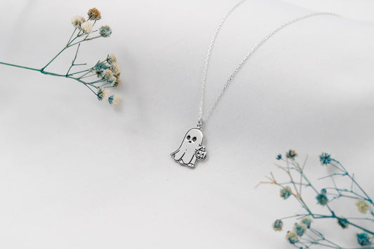 Ghost-shaped pendant necklace on a white background with dried flowers