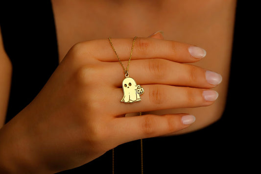 Gold necklace with a ghost pendant on a hand against a dark background