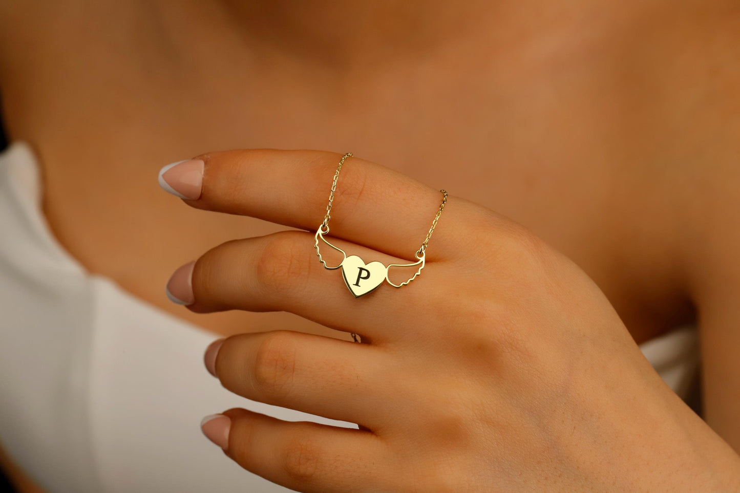 Gold necklace with a heart-shaped pendant featuring a 'P' on a hand.