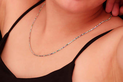 A close-up image of a person wearing a dainty multicolor necklace with round prong tennis design, featuring colorful CZ stones.