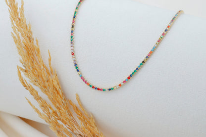 A close-up image of a dainty multicolor necklace with round prong tennis design, featuring colorful CZ stones.