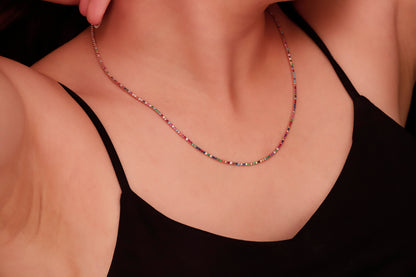 A close-up image of a person wearing a dainty multicolor necklace with round prong tennis design, featuring colorful CZ stones.