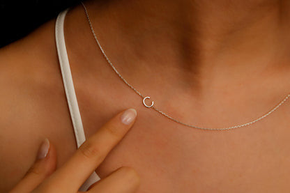 A close-up image of a custom Sideway Initial Necklace worn on a person's neck, displaying silver letter on a chain.