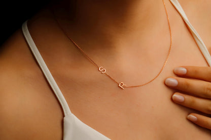 A close-up image of a custom Sideway Initial Necklace worn on a person's neck, displaying rose gold letters on a chain.
