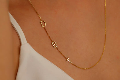 A close-up image of a custom Sideway Initial Necklace worn on a person's neck, displaying gold letters on a chain.