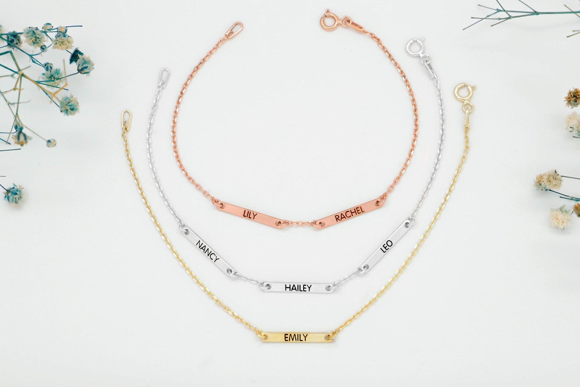 Three name bracelets in gold, rose gold, and silver on a white background with small flowers.