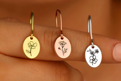 A close-up image of a person holding 3 small hoop earrings with a dangling flower-shaped charm.