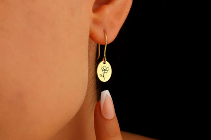 A close-up image of a person wearing a small gold-colored hoop earring with a dangling flower-shaped charm.
