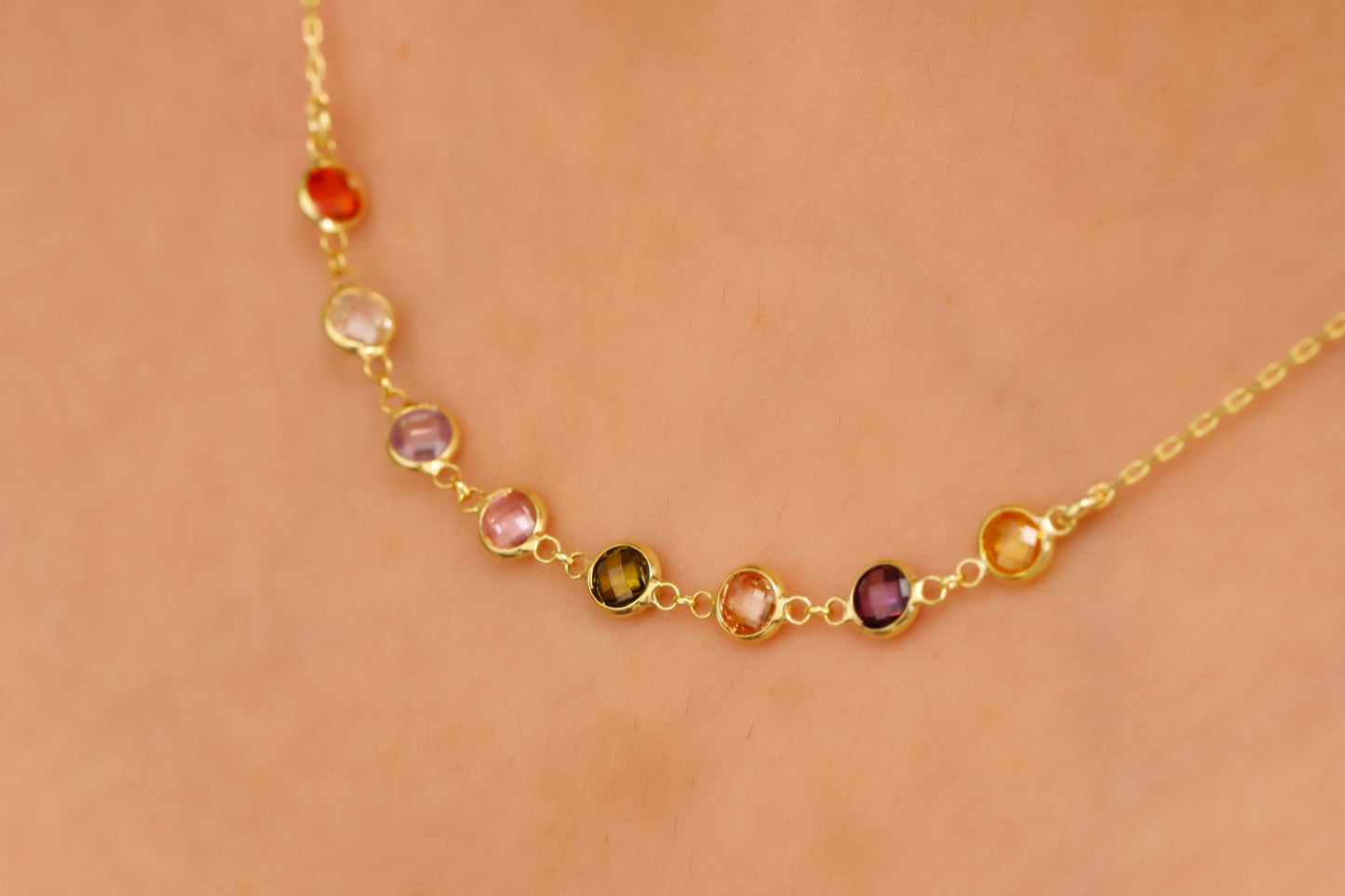 Gold necklace with multicolored gemstones on a person's neck against a beige background